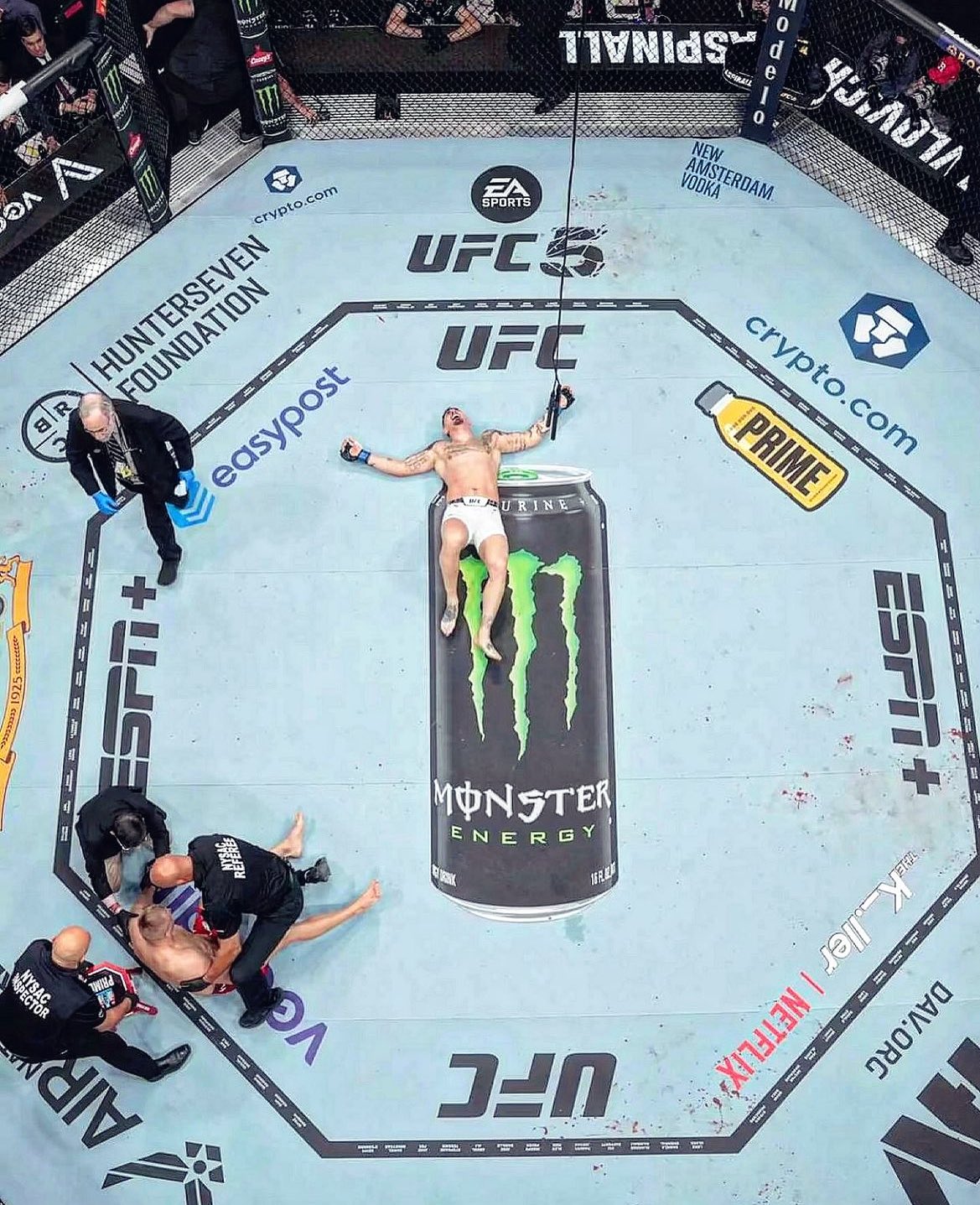 Tom Aspinall comemorando aliviado a sua vitória enquanto Sergei Pavlovich recebe atendimento médico após o nocaute. (Foto: Josh Hedges | Crédito: Zuffa LLC via Getty Images | Reprodução: @UFC)