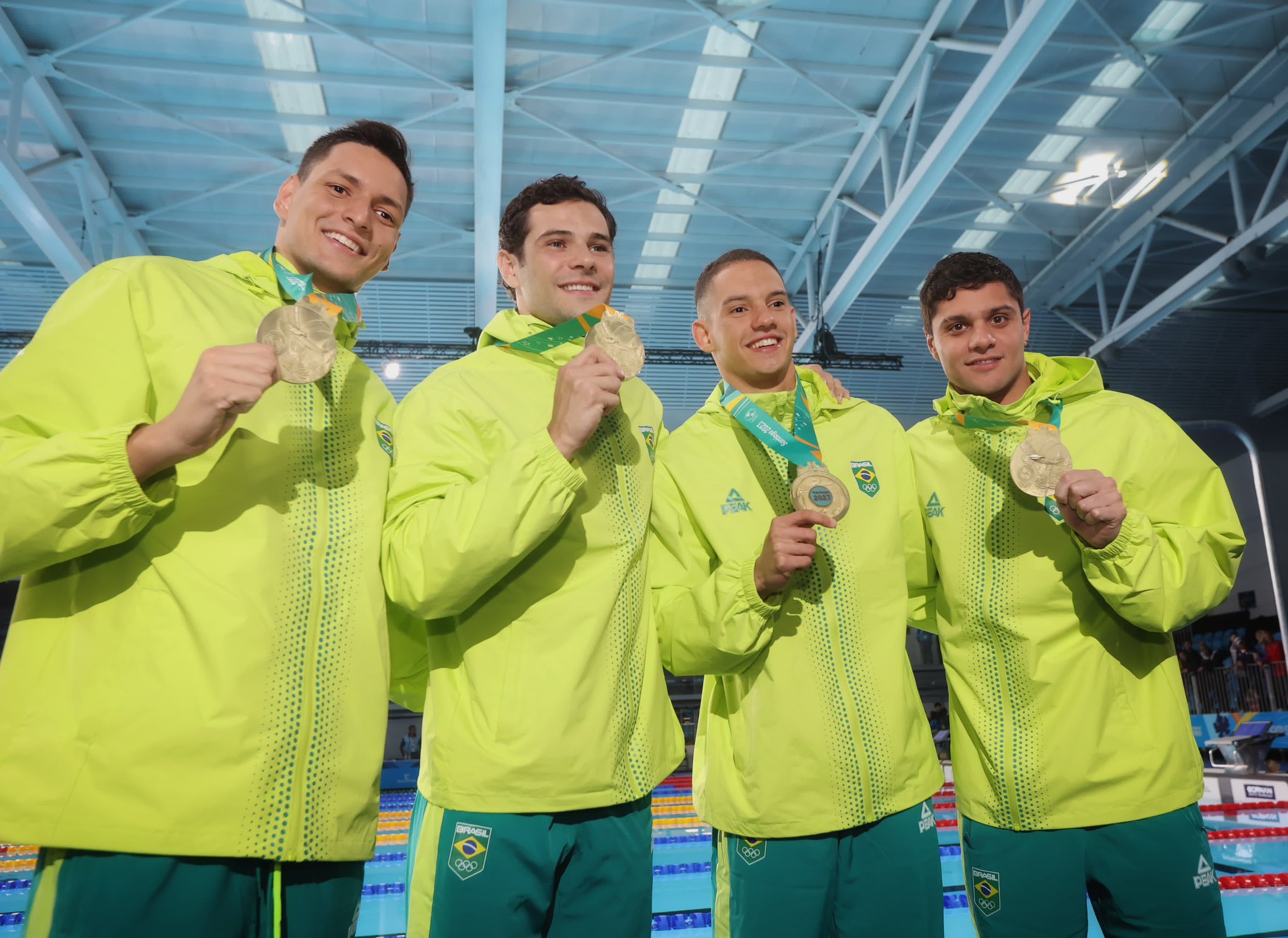 Atletas da seleção brasileira, usando uniforme verde e amarelo, segurando a medalha de ouro
