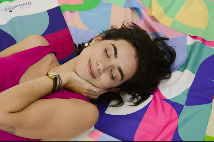 Lara deitada em meio a tecidos coloridos