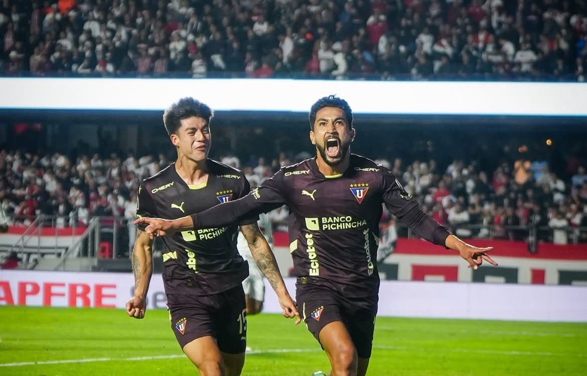 Jogadores do LDU correndo em direção a câmera enquanto comemoram gol