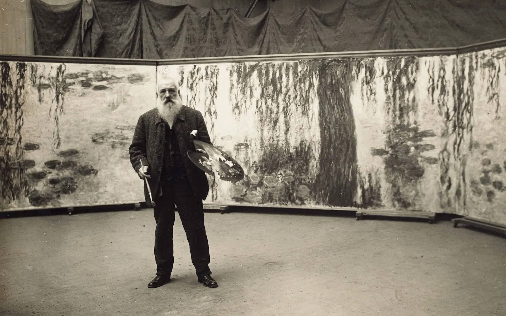 Monet em seu estúdio posando ao lado de algumas de de suas famosas pinturas da série "Nenúfares. Fonte: Cultura Colectiva