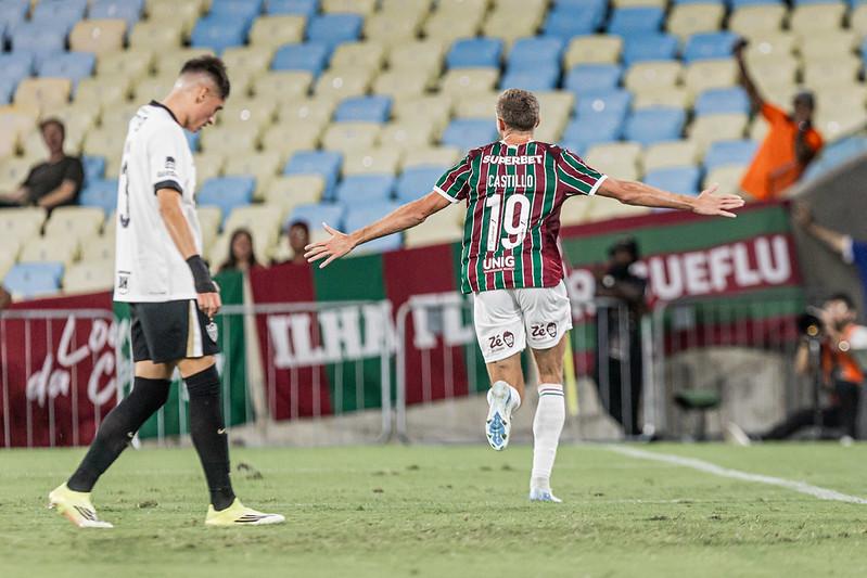 A imagem mostra Castillo de costas correndo com os braços abertos. Ao fundo está a arquibancada vazia. Do lado esquerdo, há um jogador do Atlético-MG de cabeça baixa.