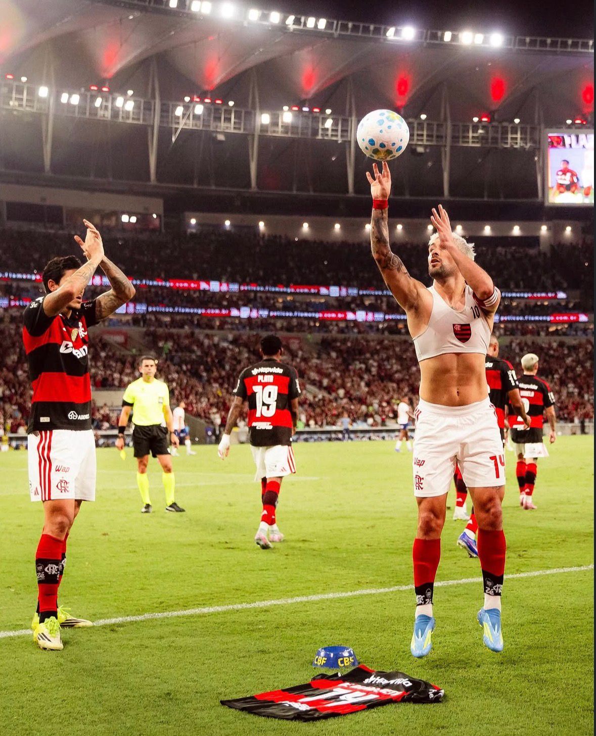 A imagem mostra Arrascaeta, do Flamengo, comemorando arremessando a bola como se fosse no basquete. Ao lado esquerdo está Pedro, do Flamengo, batendo palmas.