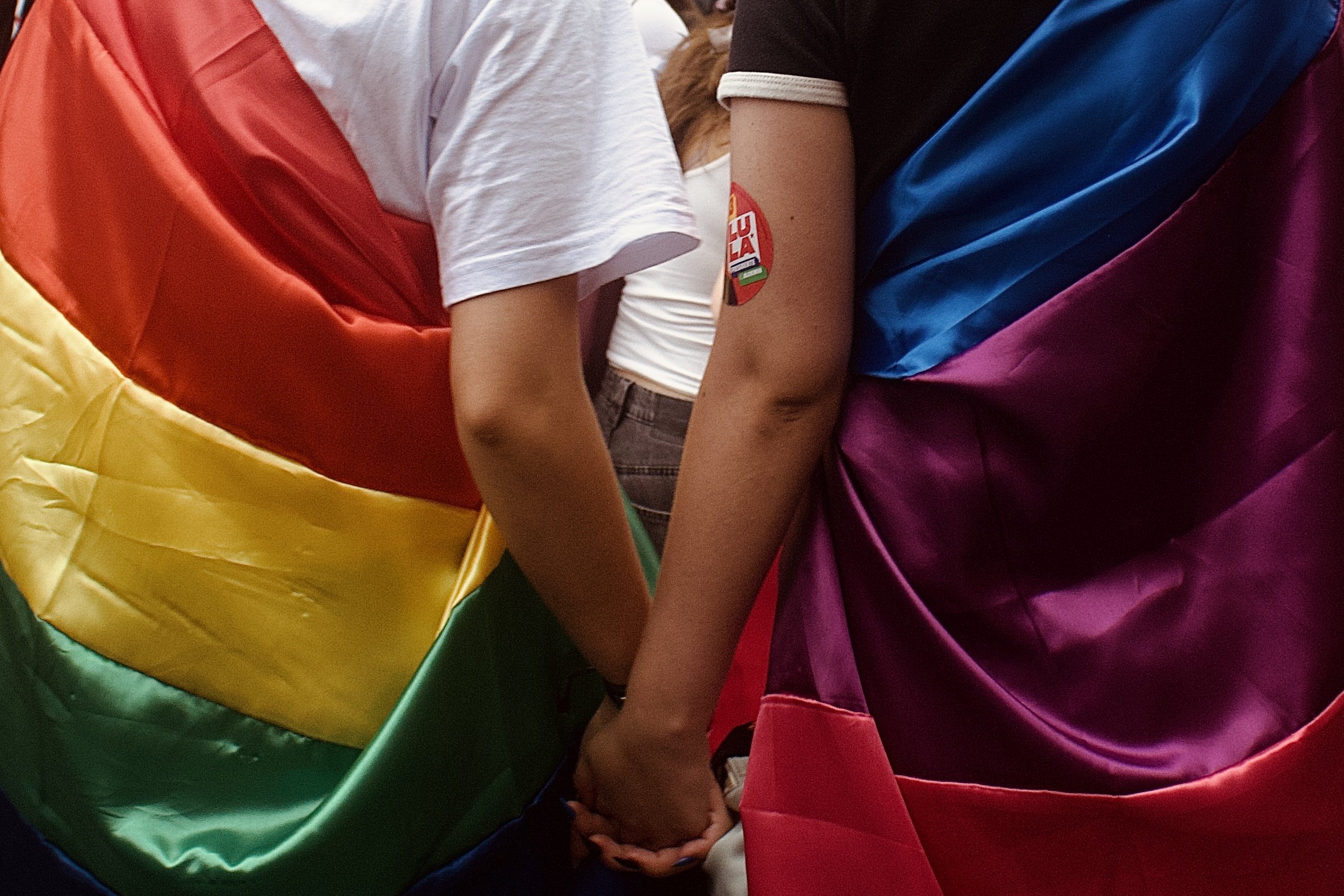 Casal de mãos dadas com bandeira LGBTQI+ sobre as costas 