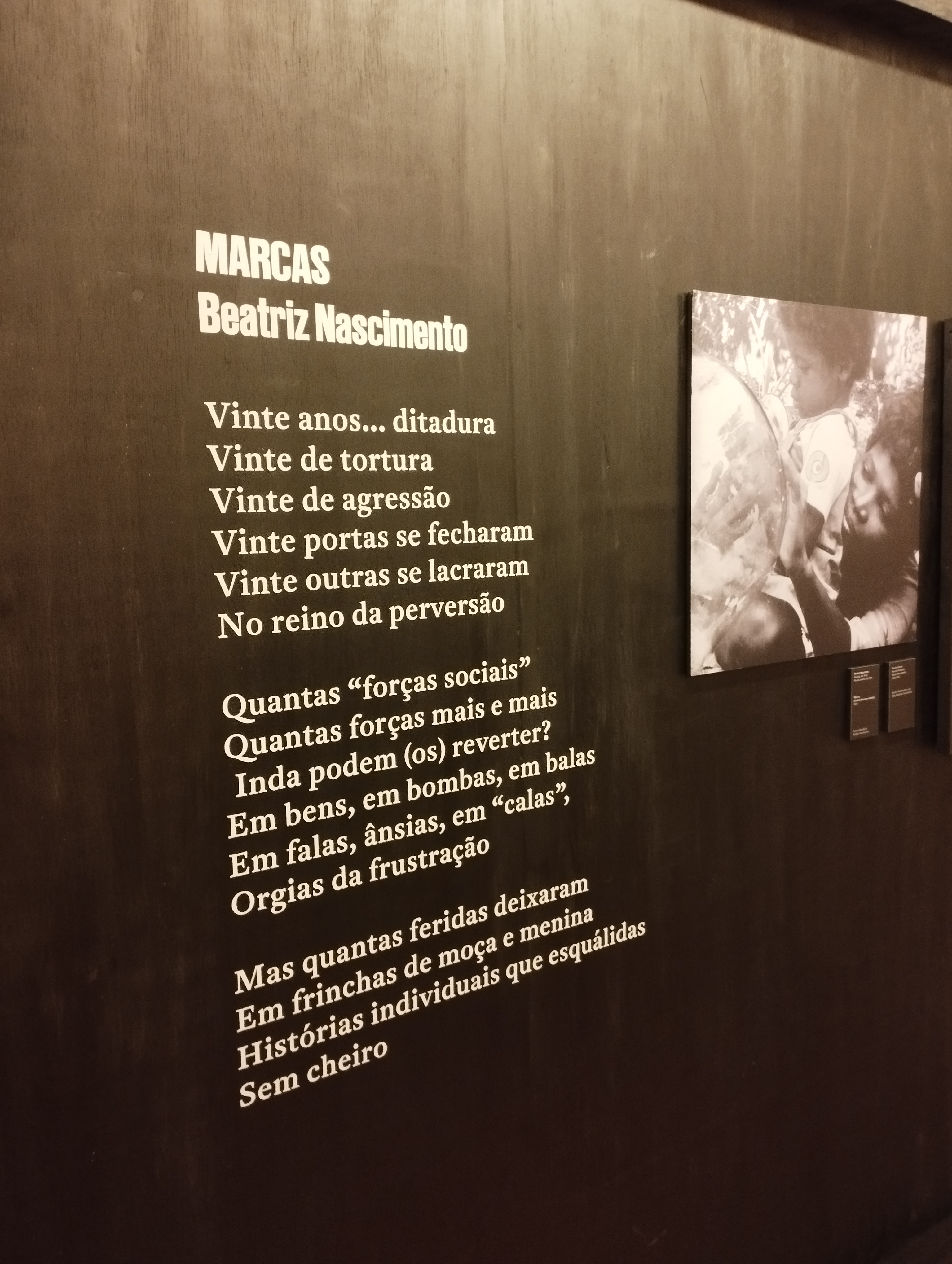 Poema "Marcas" com letras brancas, de Beatriz Nascimento na parede preta da exposição