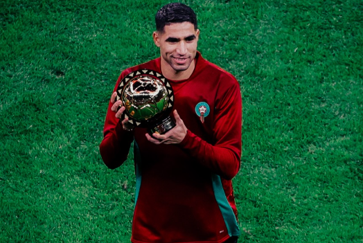 Jogador Hakimi em campo segurando prêmio de melhor jogador africano e usando uniforme de Marrocos.