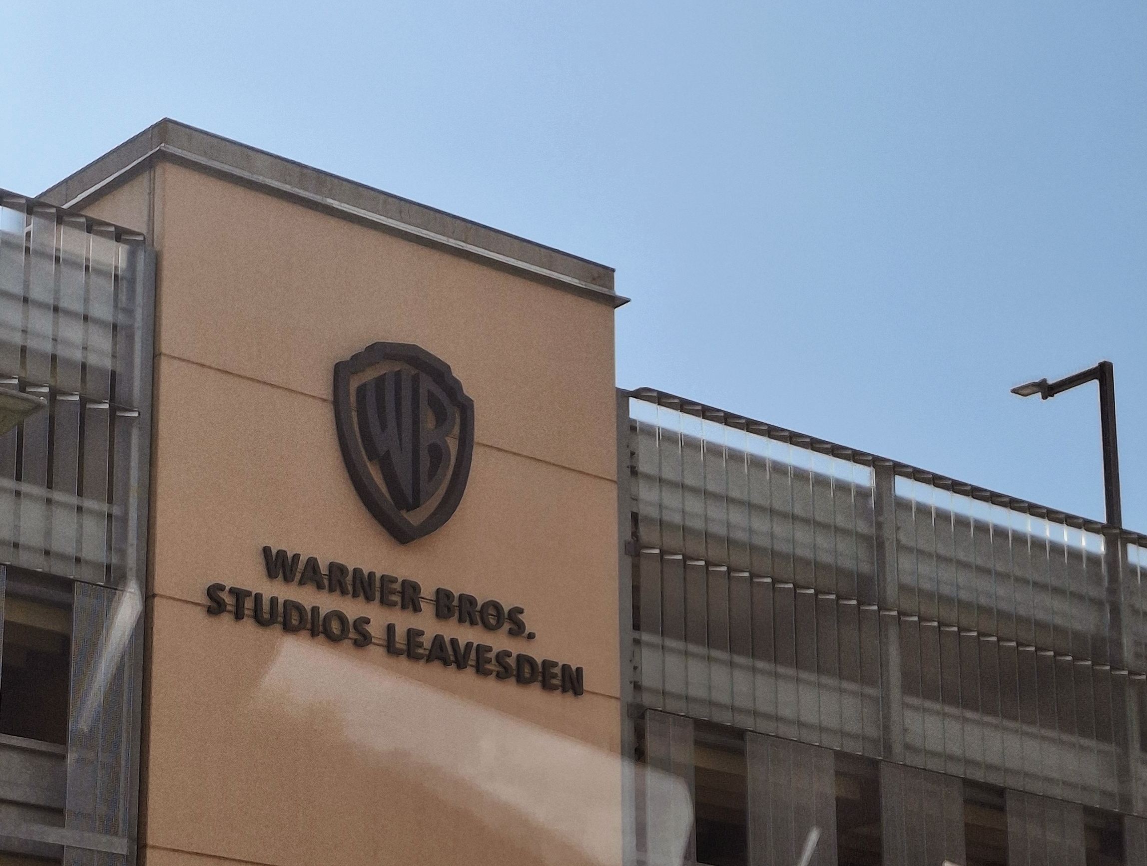Fachada do prédio dos Warner Bros. Studios Leavesden, com o logotipo da Warner Bros. em destaque na parede bege.