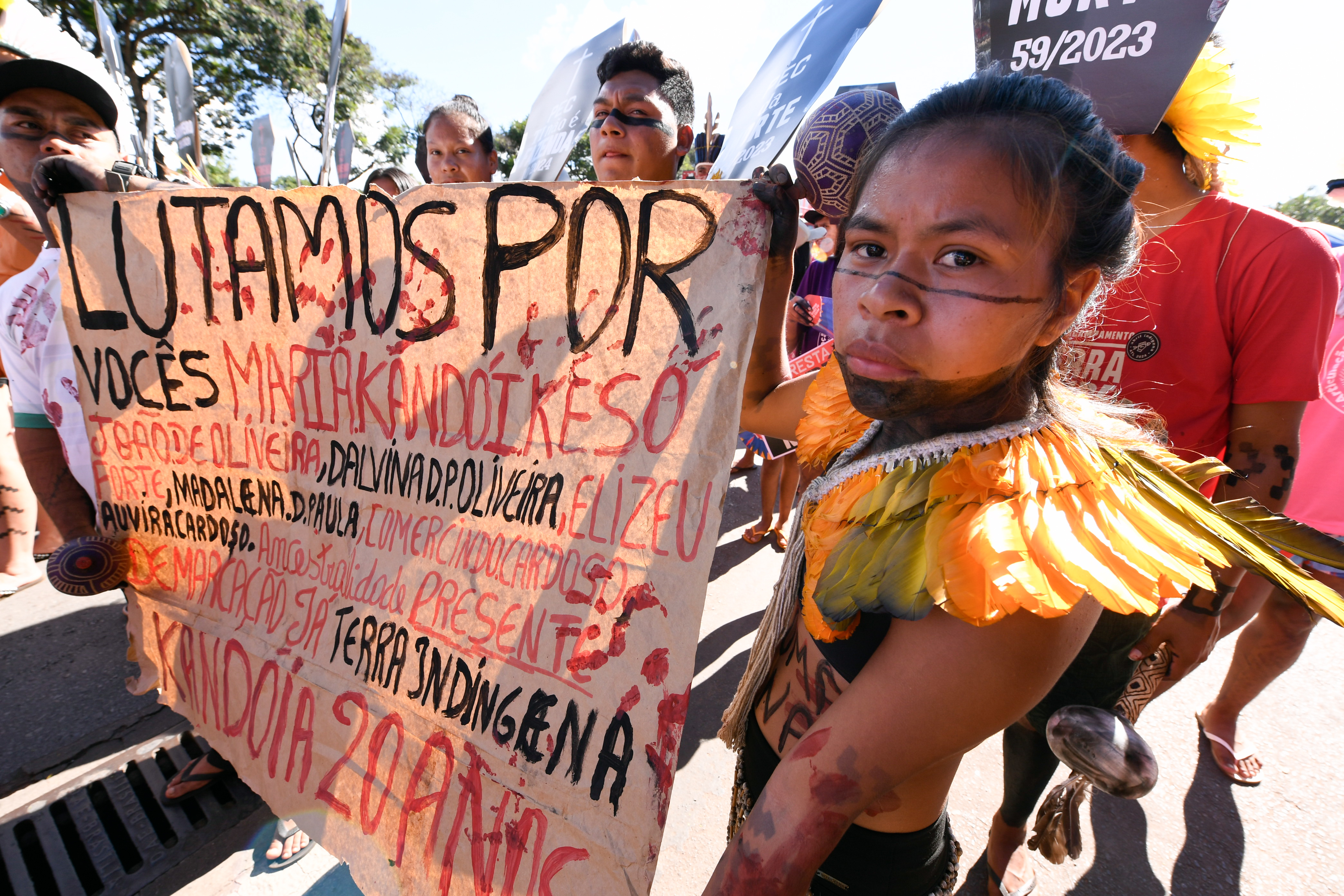 Mulher indígena segurando um cartaz na marcha do Acampamento Terra Livre pedindo justiça pelos indígenas mortos em conflitos de demarcação de terra.