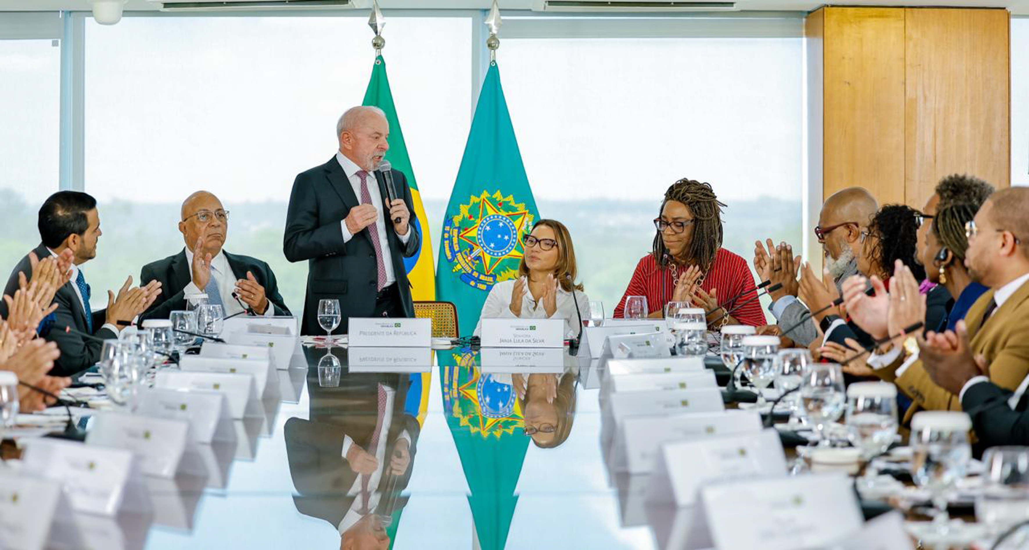 diversos lideres políticos e religiosos com vestimentas formais ouvindo o presidente lula falar no microfone 