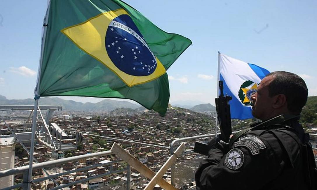 Legenda: Policiais hasteiam bandeira do Brasil e do estado do RJ após invasão ao Complexo do Alemão. Reprodução: Bruno Gonzalez