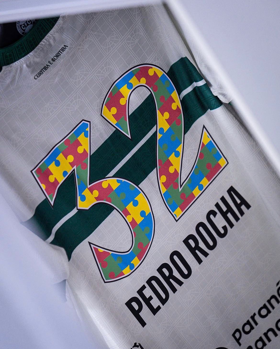 A imagem mostra a camisa de Pedro Rocha, do Coritiba, com o número 32 formado pelo símbolo do autismo, em quebra cabeça nas cores vermelho, azul, amarelo e verde.