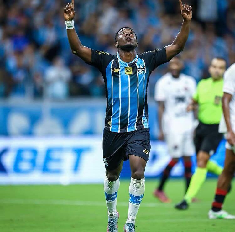 A imagem mostra o jogador Amuzu, do Grêmio, comemorando o gol com as mãos apontadas para o céu