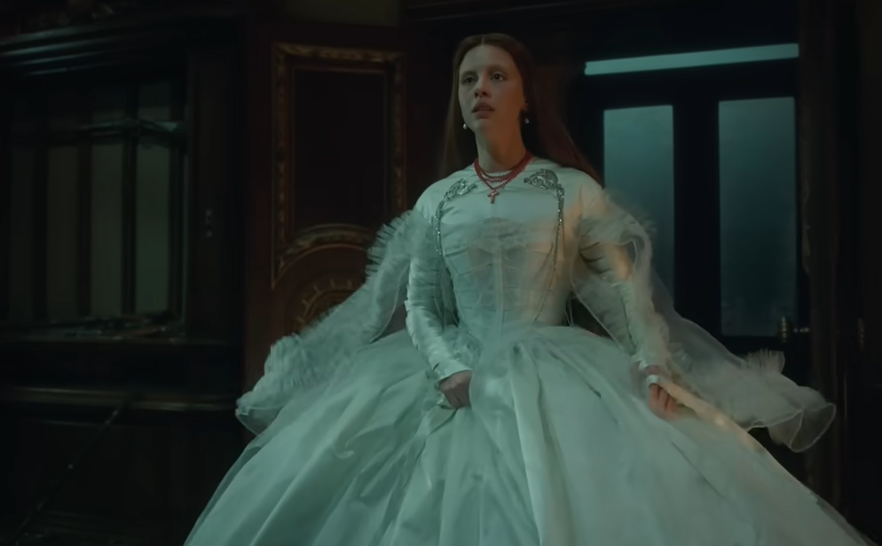 Foto: Personagem Elizabeth usa vestido volumoso branco em meio a uma sala escura.