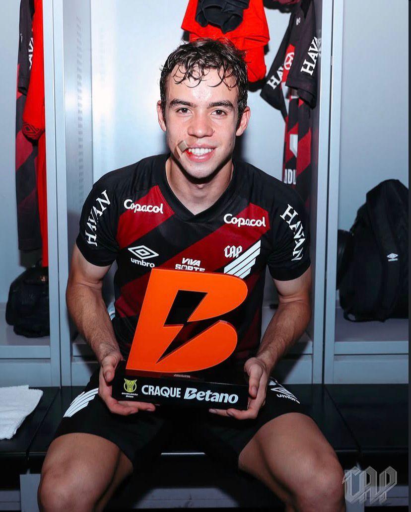 A imagem mostra Dudu, do Athletico-PR no vestiário com o troféu de melhor da partida.