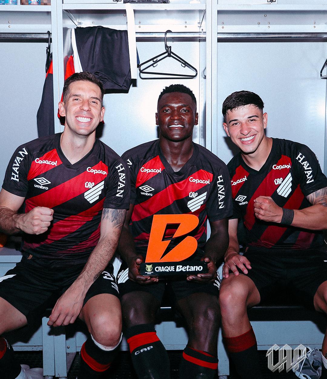 A imagem mostra da esquerda para a direita os jogadores Aguirre, Viveros e Esquivel sentados, posando para a foto. No colo de Viveros está o troféu de melhor da partida. Eles estão no vestiário.