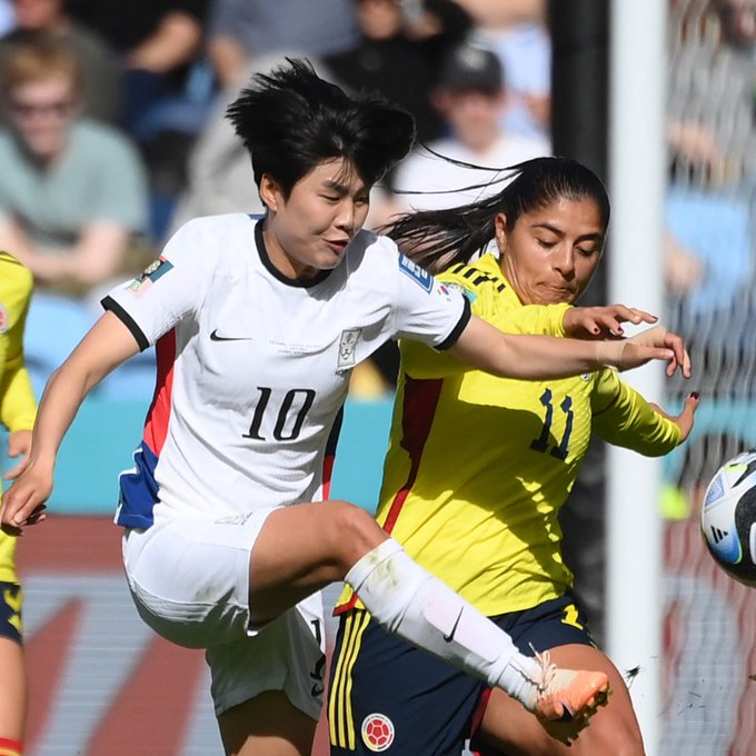 Disputa de bola entre a coreana Ji So-yun e a colombiana Catalina Usme em frente à entrada da área.