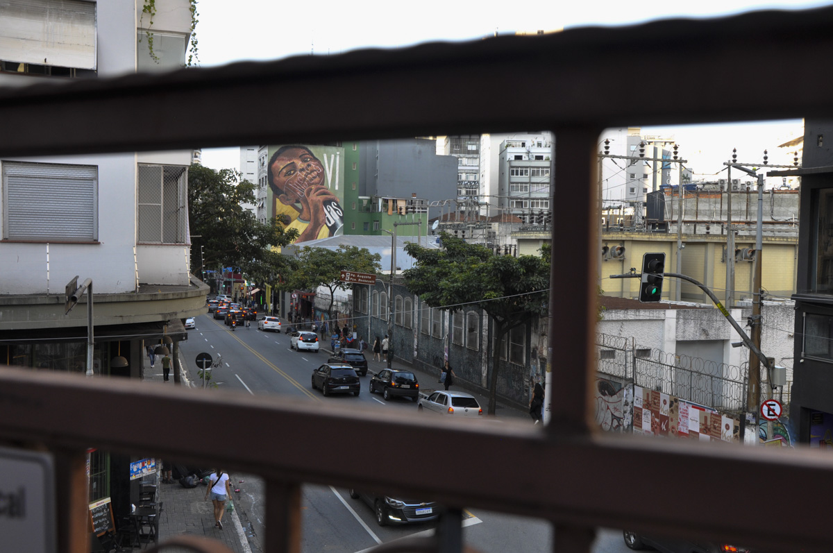 Foto da Rua Augusta tirada de cima. Ao mesmo tempo que mostra o trânsito ao fundo há um grafite de um menino negro que em seu rosto está escrito justiça