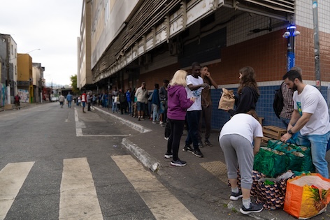 Pessoas em situação de vulnerabilidade formam fila para receber kits entregues por voluntários na Lapa