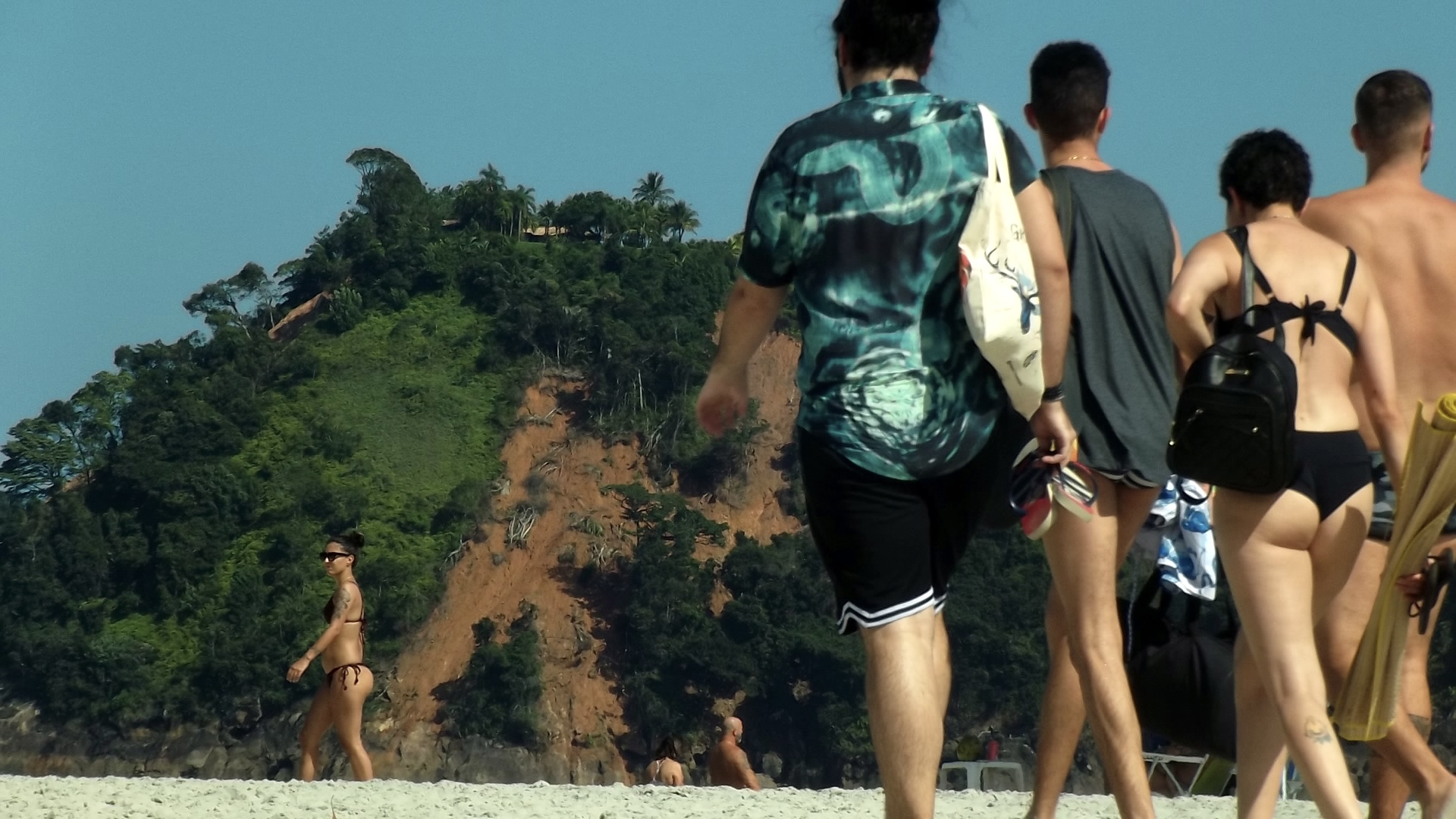 Família andando na praia com os morros deslizados como paisagem