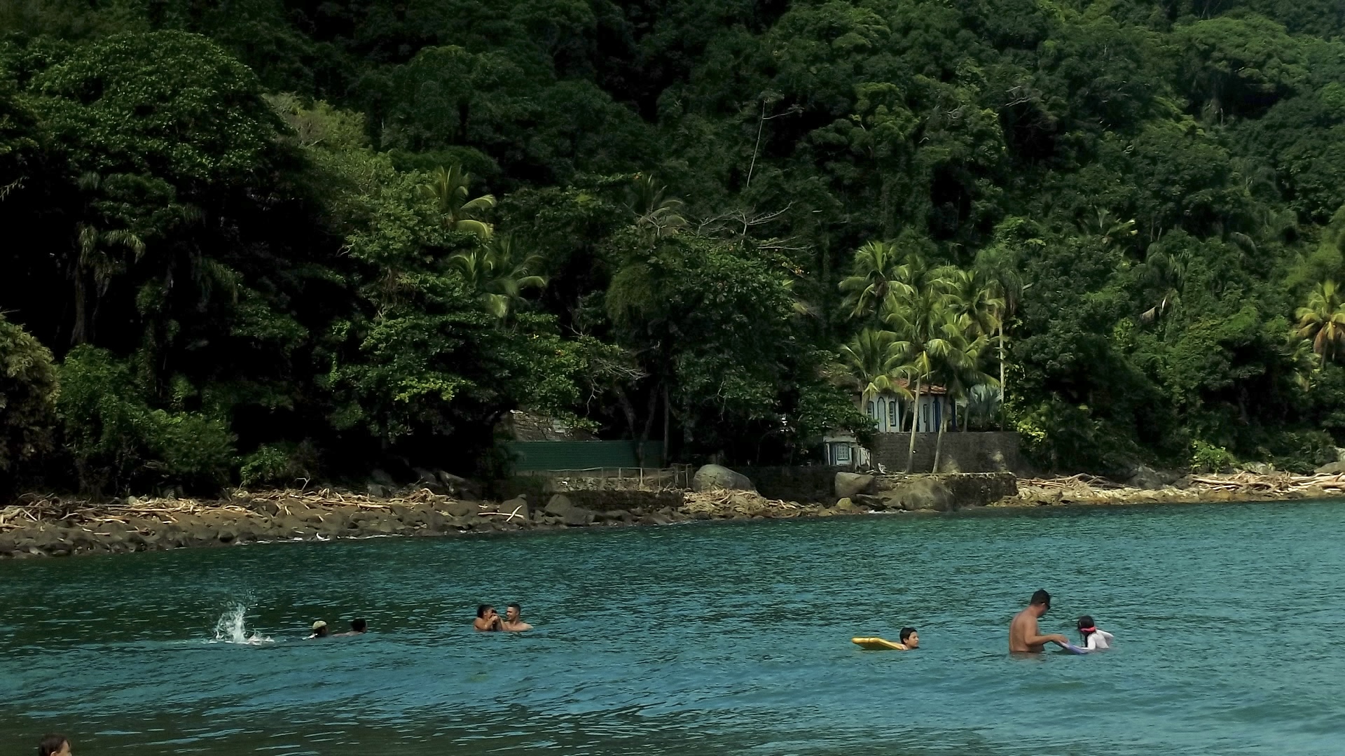 Pessoas brincando no mar com uma casa interditada atrás