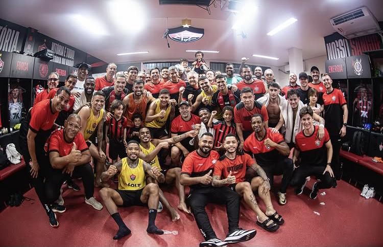 A imagem mostra o elenco e comissão técnica do Vitória posando para a foto no vestiário.