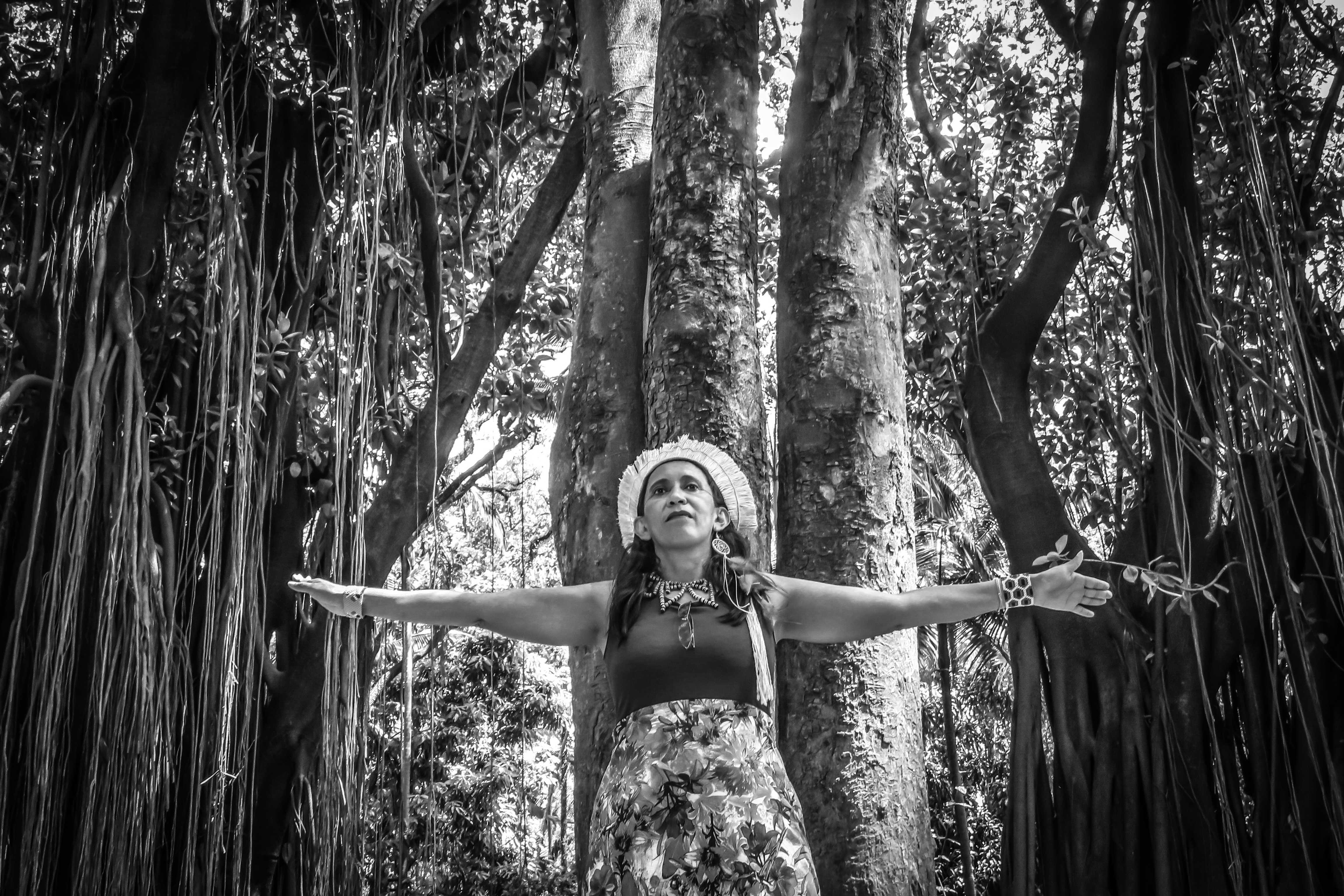 mulher indígena de braços abertos, árvore de fundo 