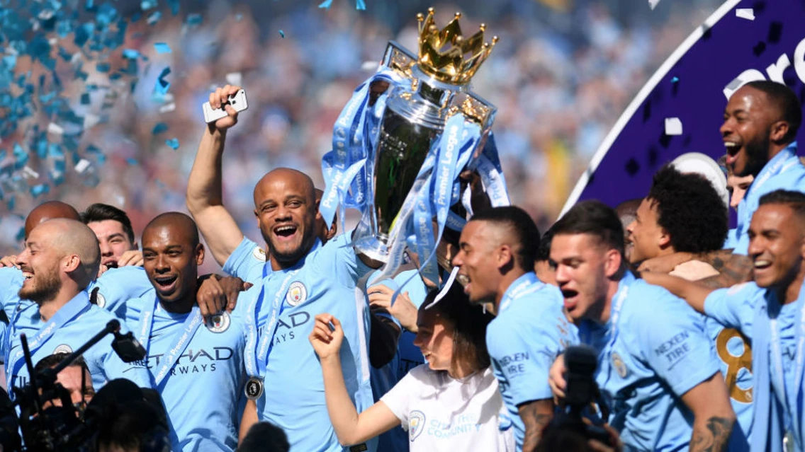 A imagem mostra Vincent Kompany com a taça da PL 2016 e outros jogadores do City comemorando o título na época