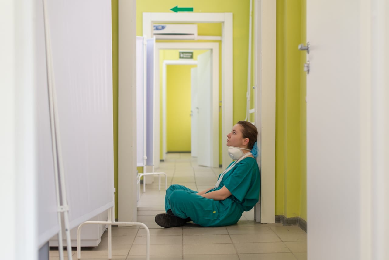 enfermeira uniformizada sentada ao chão e olhando para cima dentro de corredor hospitalar