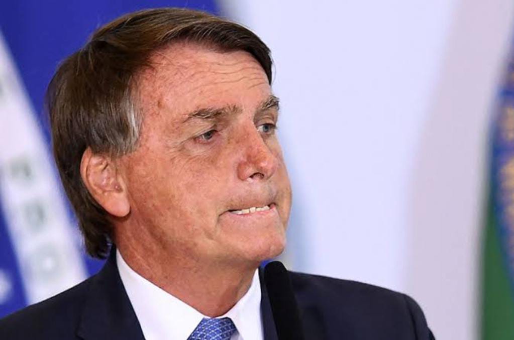 Reprodução: AFP | Bolsonaro morde os lábios em frente à bandeira do Brasil