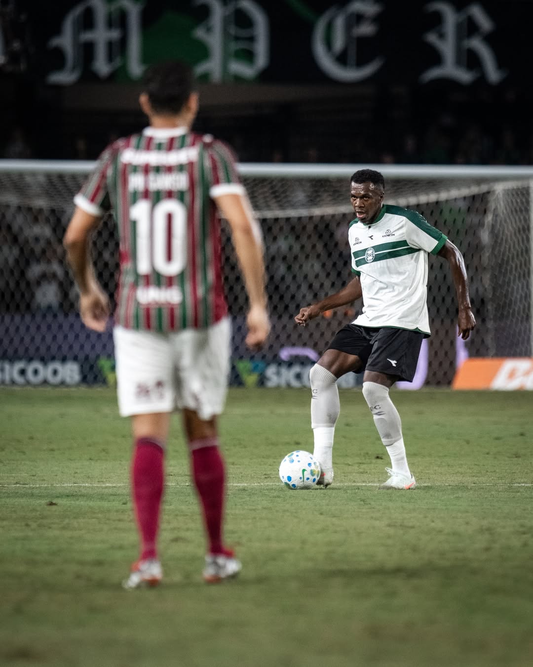 A imagem mostra um jogador do Coritiba chutando uma bola. 