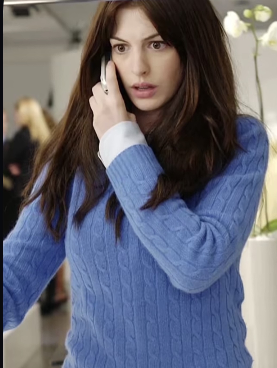 Anne Hathaway no primeiro filme de Diabo Veste Prada usando um casaco azul enquanto fala no telefone 