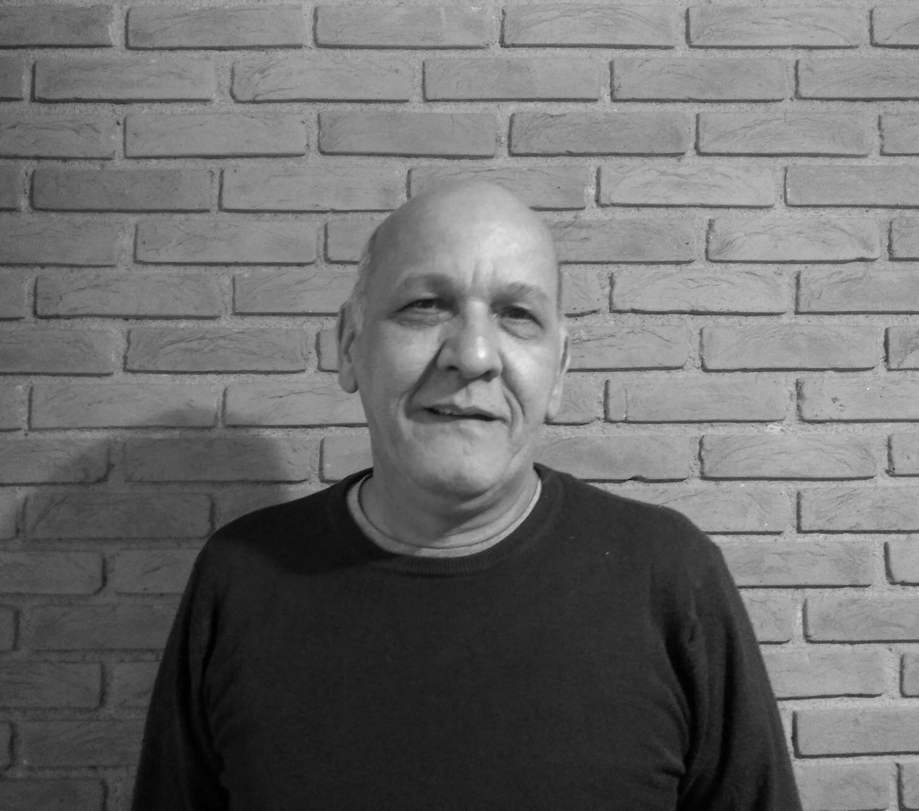 Uma fotografia em preto e branco de meu tio Claúdio sorrindo atrás de uma parede de tijolos