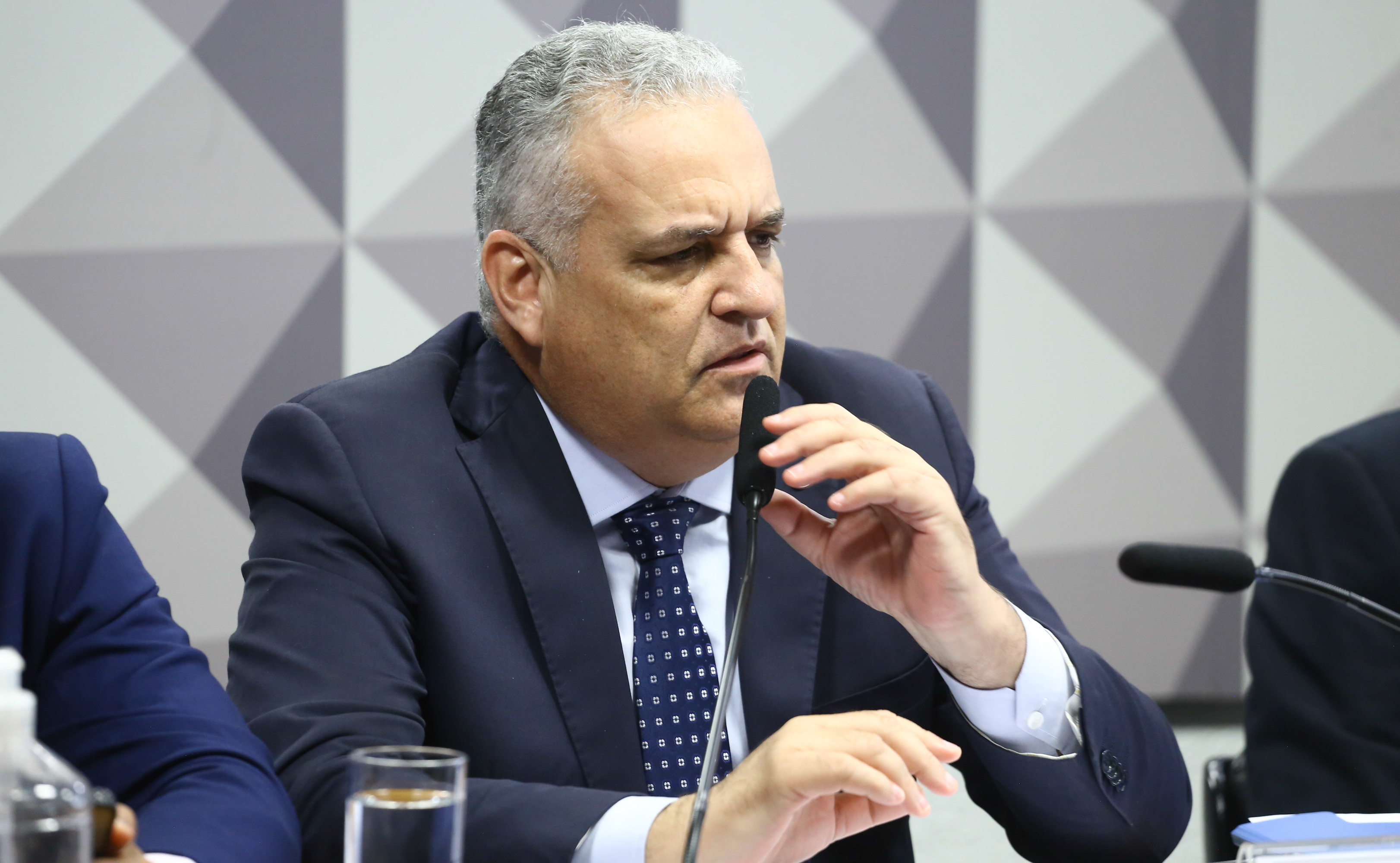 ​​​​Homem de terno fala ao microfone durante sessão de comissão no Congresso, sentado à mesa com copo de água à frente.