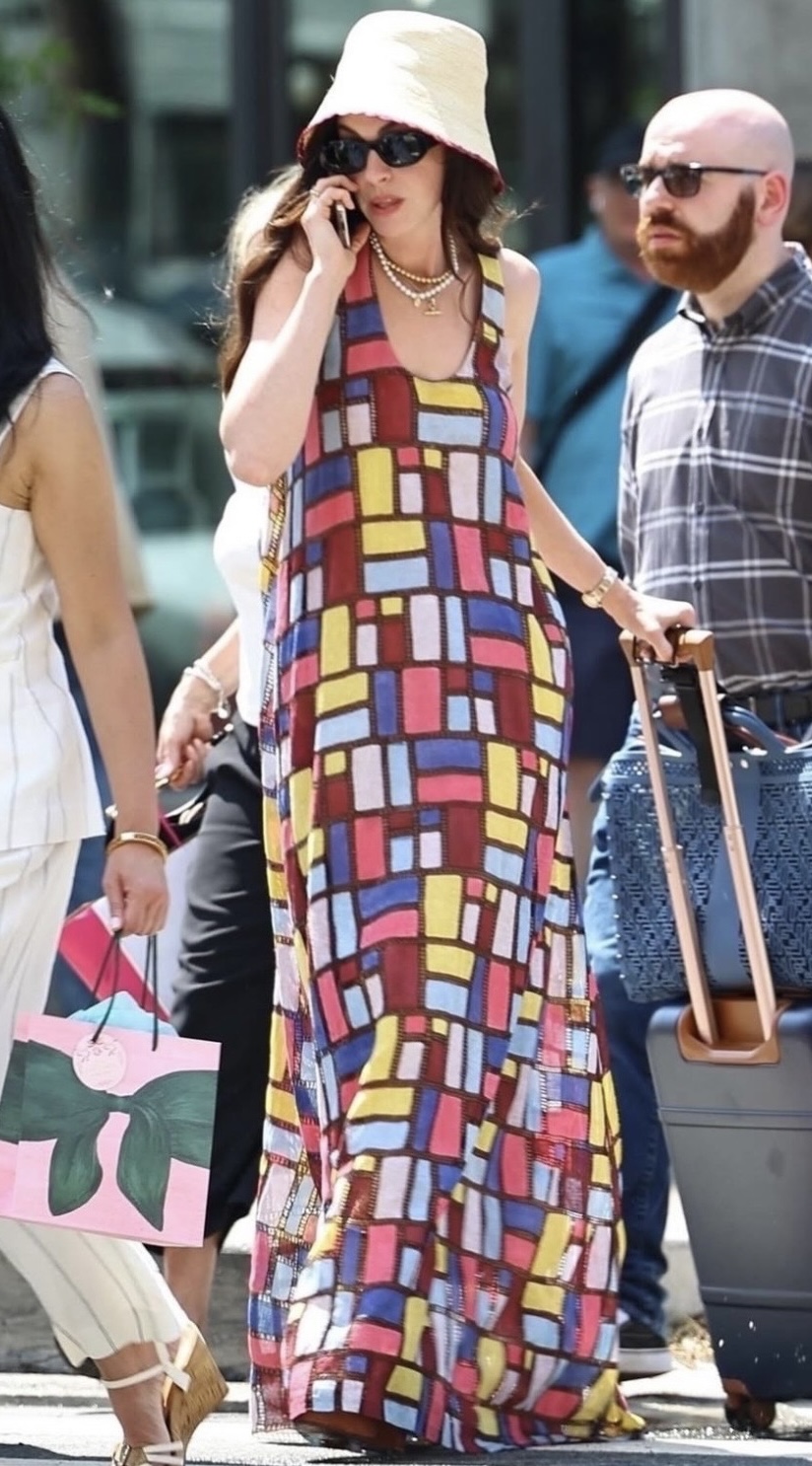 Anne Hathaway como Andrea Sachs andando pela calçada, falando no telefone, usando um vestido colorido 