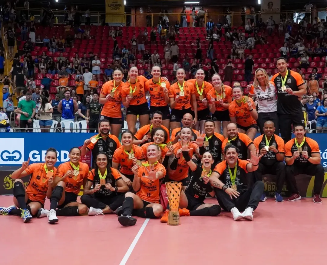 A imagem mostra todo o elenco e comissão técnica do Osasco com suas medalhas. A frente no chão está o troféu da Copa Brasil de Vôlei. Ao fundo está a arquibancada.