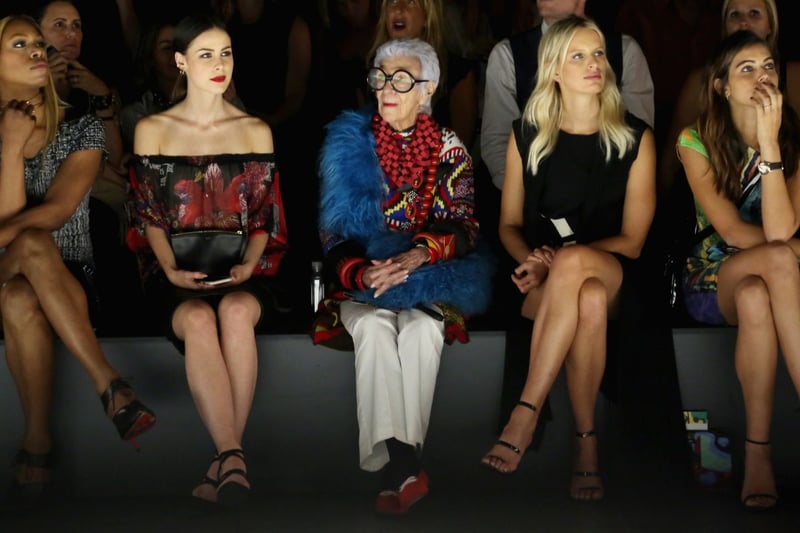 A americana, Iris Apfel, sentada na primeira fileira durante a semana de moda de Nova York em 2016. Seu estilo é contrastante com todos à sua volta.