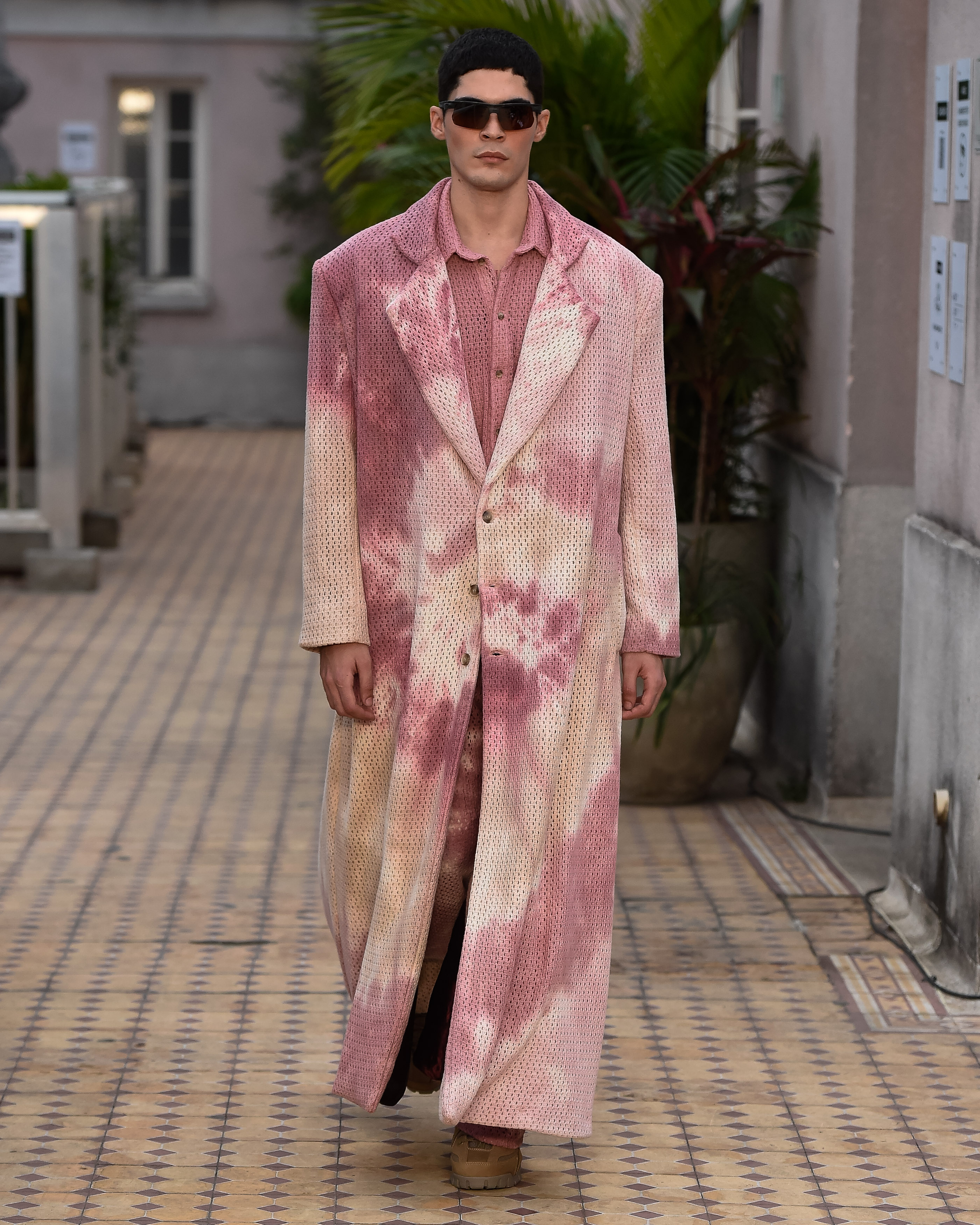 Modelo com casaco tie-dye em tons rosas e um óculos marcando o look.