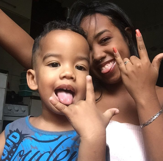 A imagem mostra Kelly e seu filho pequeno fazendo o sinal do rock com as mãos e sorrindo