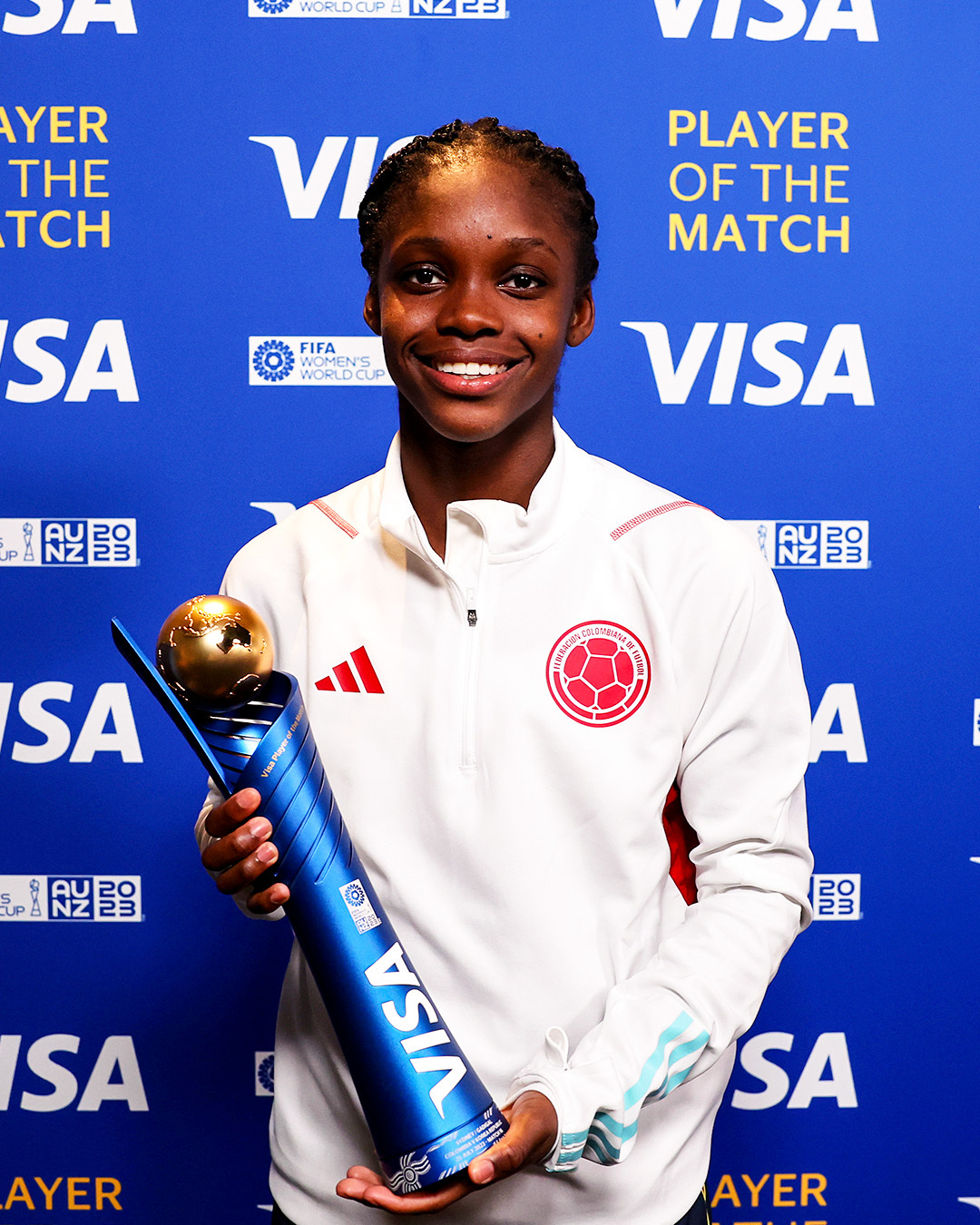 Linda Caicedo segurando um troféu azul e dourado, de melhor jogadora da partida, na zona mista, após o jogo.