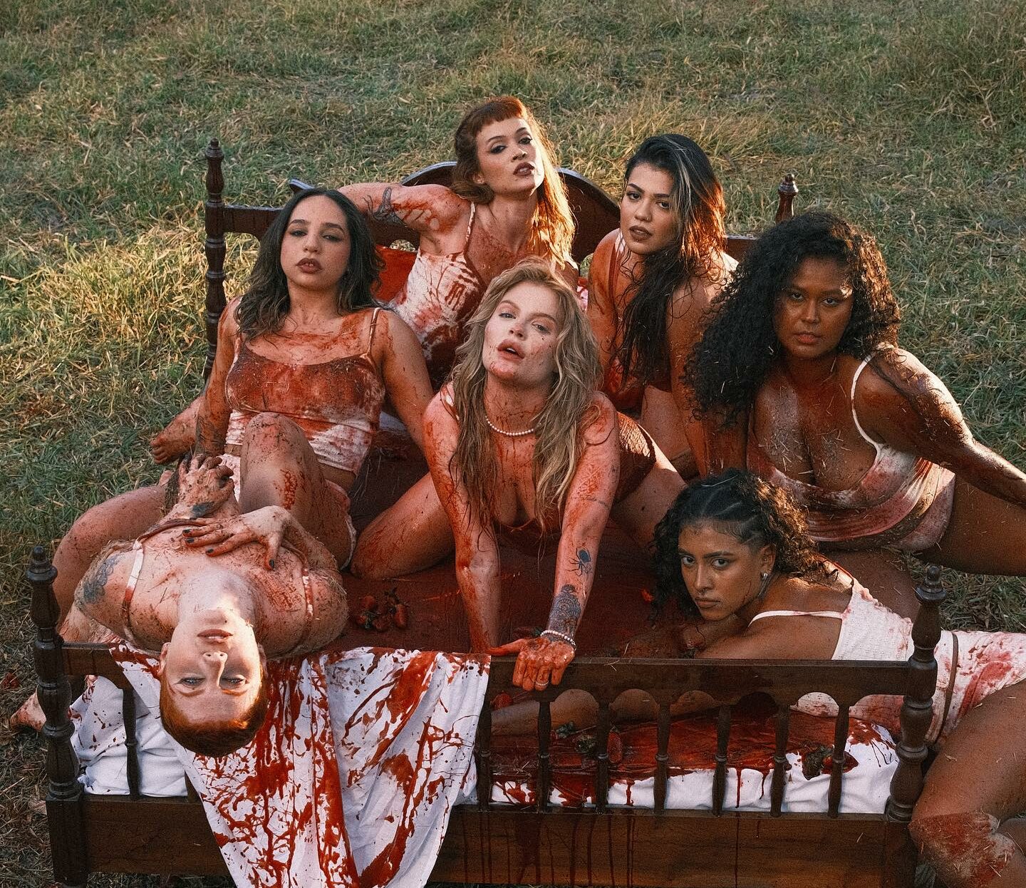 Luísa no clipe "Campo de Morango" em cima de uma cama coberta de tinta vermelha com dançarinas ao seu lado