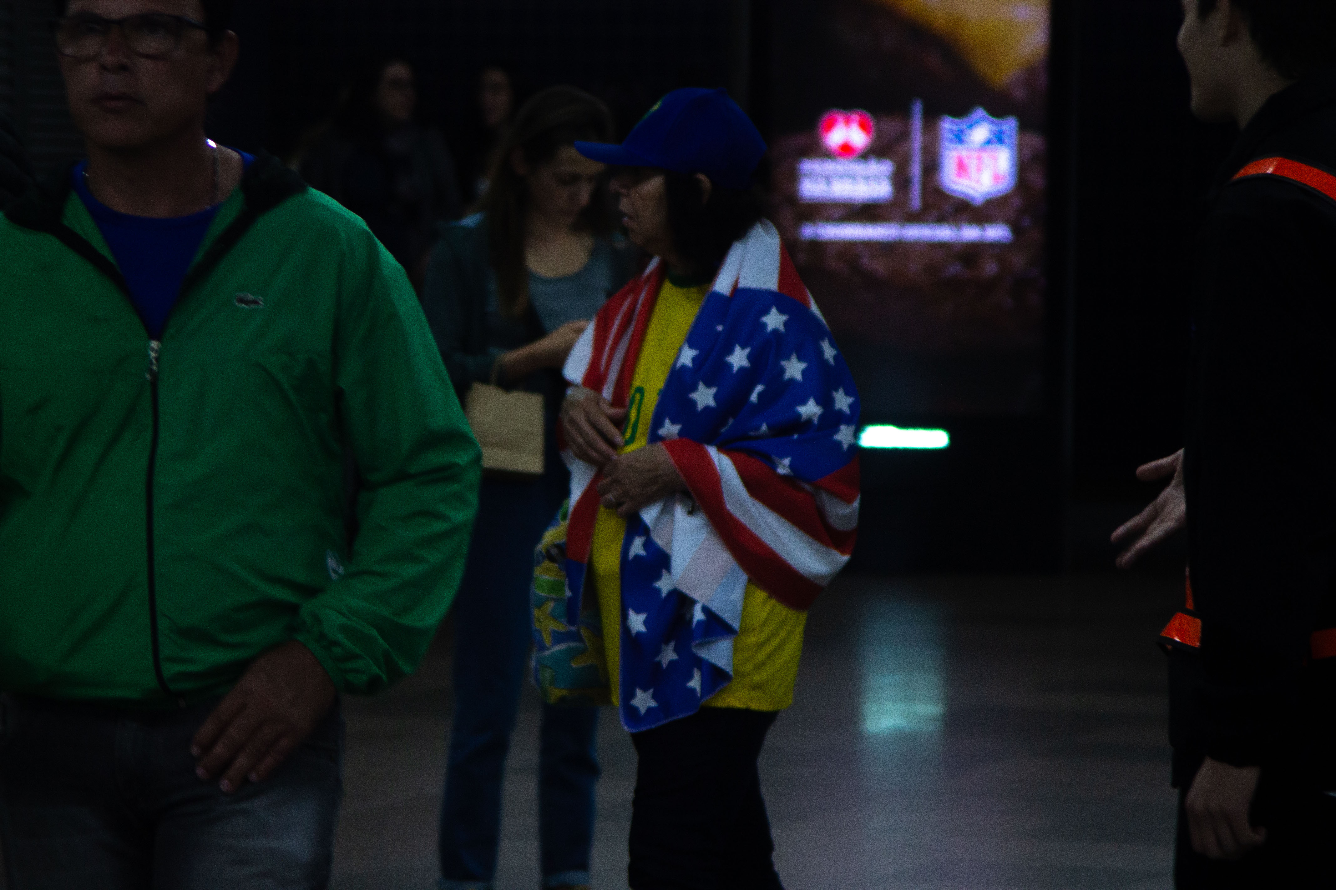 Uma mulher no Metrô Trianon Masp com uma camisa da seleção brasileira com uma bandeira dos Estados Unidos por cima / Foto: Rafael Pessoa