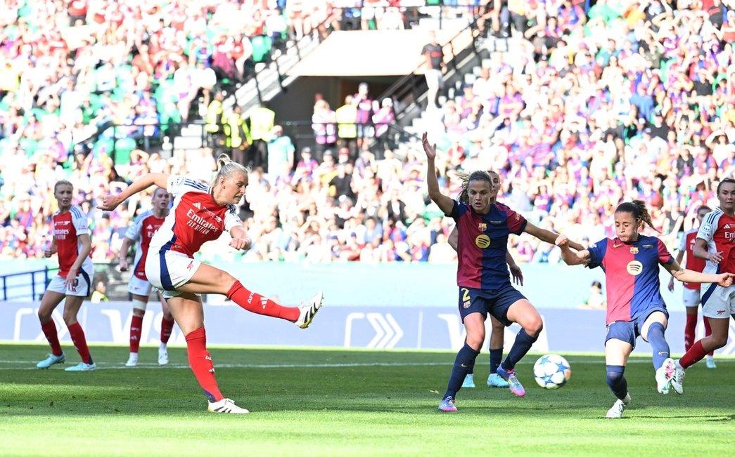 A imagem mostra à esquerda a jogadora Blackstenius com a perna direita erguida após chutar a bola. No lado direito está a bola indo em direção ao gol e duas defensoras do Barcelona que não alcançaram a bola.