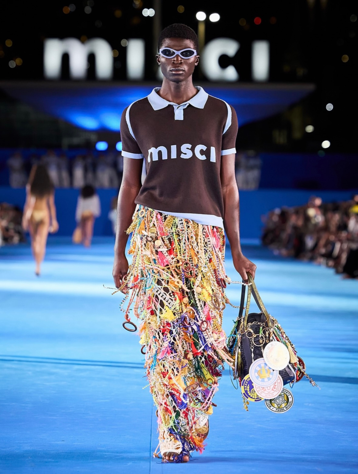 Modelo com calça colorida e volumosa com blusa escrito "misci"