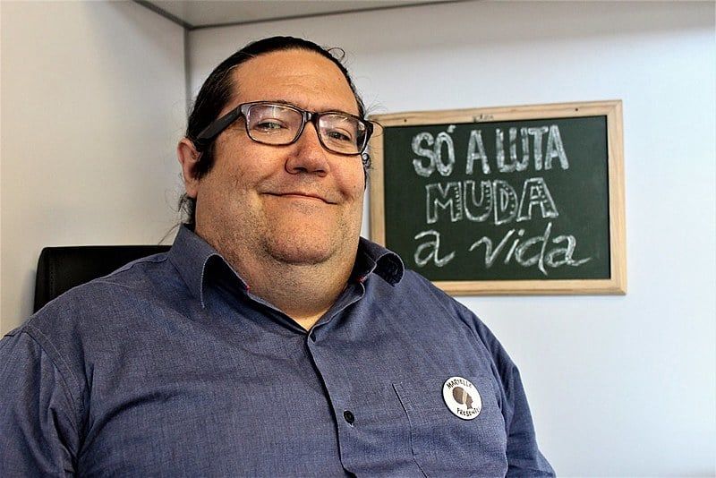 Foto de Tarcísio Motta feita pelo Brasil de Fato, atrás do candidato temos um quadro de giz com a frase "Só a luta muda a vida".