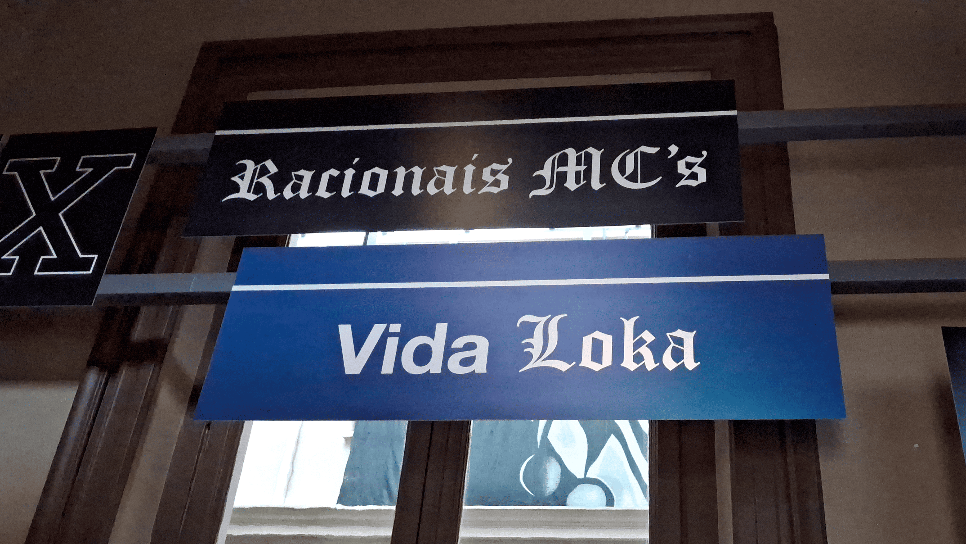 A imagem apresenta três placas, em sequência, com os dizeres "X", "Racionais MC's" e "Vida Loka".