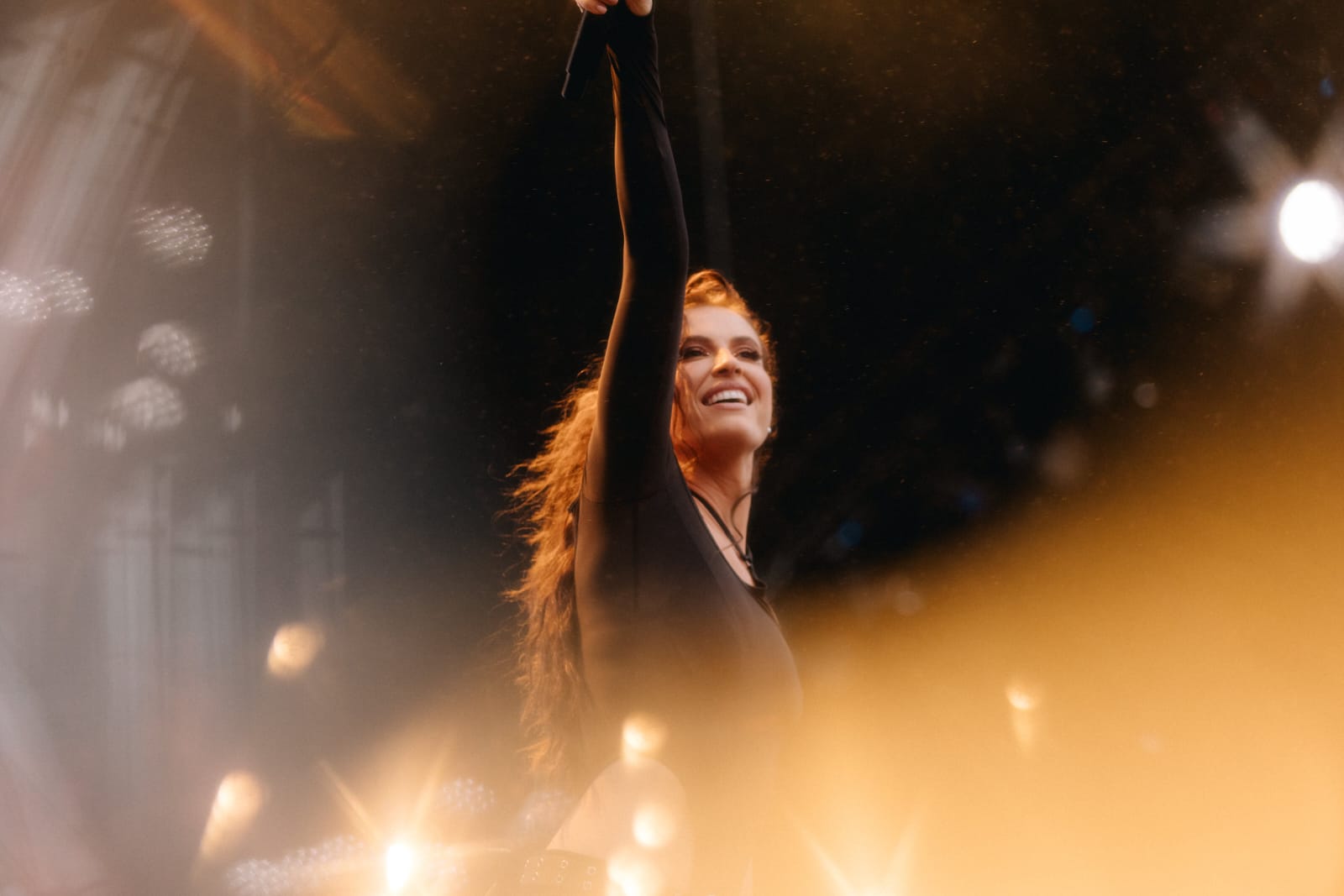Cantora americana Fletcher de lado sorrindo com o braço direito para cima segurando o microfone no Lollapalooza Brasil 2024. Ela veste um traje todo preto de mangas compridas