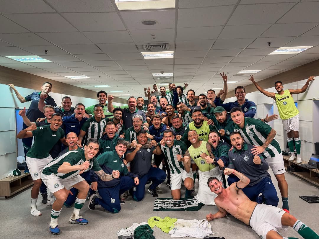 A imagem mostra o elenco e comissão técnica do Coritiba comemorando a vitoria no vestiário.