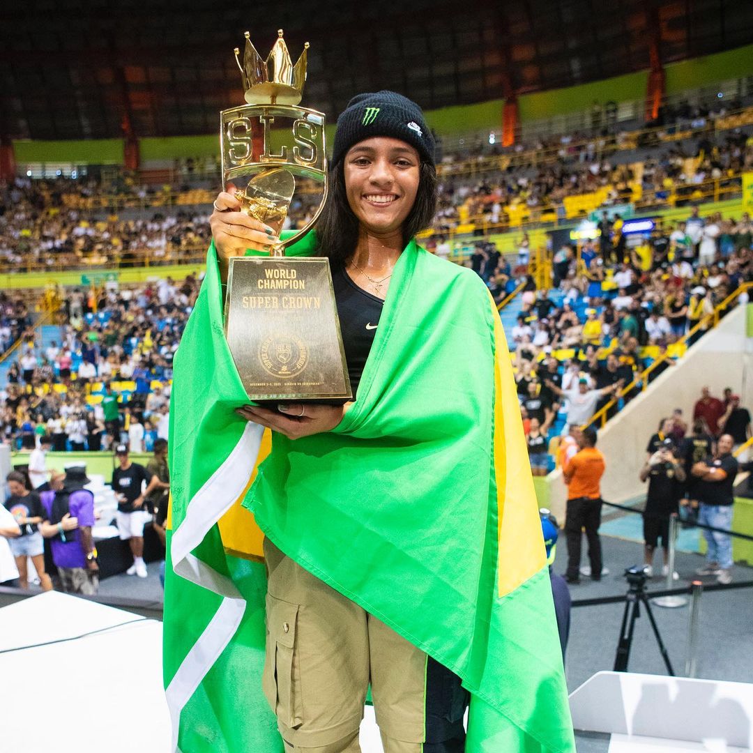 Rayssa Leal com a bandeira do Brasil nas costas enquanto segura o troféu de campeã