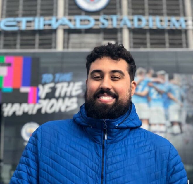 Rapaz com cabelo curto e barba, sorrindo de frente para a camera