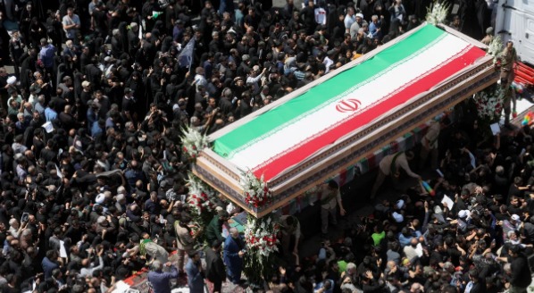 Vista do caixão de Ebrahim Raisi visto de cima, está coberto por uma bandeira do Irã. Uma multidão cerca o caixão.